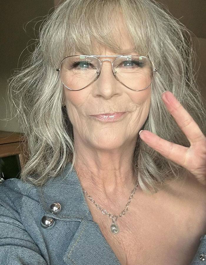 Jamie Lee Curtis close-up selfie wearing glasses and a denim jacket making a peace sign in a casual setting. Jamie Lee Curtis close-up selfie wearing glasses and a denim jacket making a peace sign in a casual setting.
