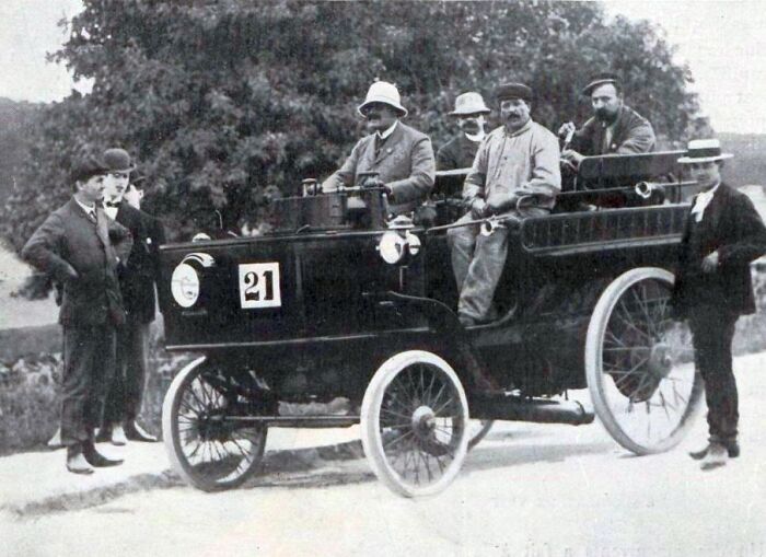 Early 20th century photo of a wild first car with men in period attire showcasing vintage automotive design.