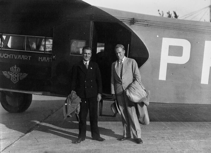 Two well-dressed men standing by a vintage airplane, capturing the era when flying was pure glamour.