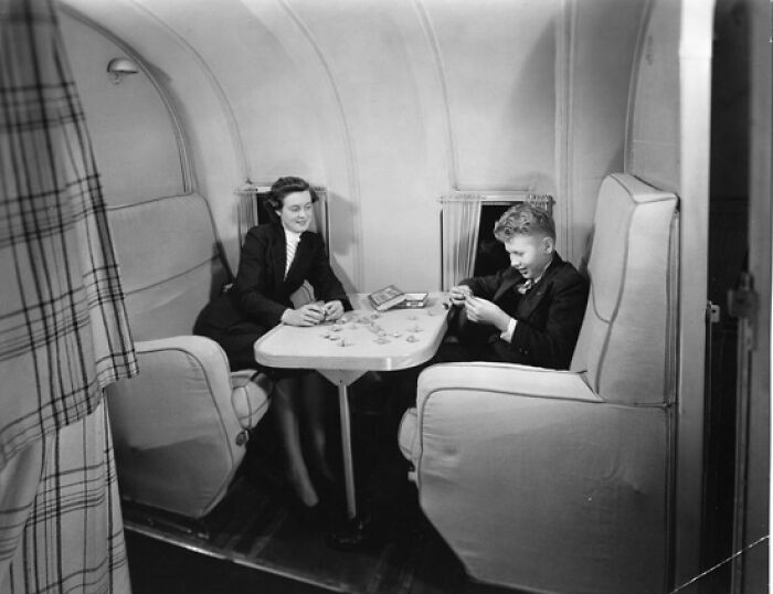 Two passengers in elegant attire playing cards in a vintage airplane cabin showing flying glamour era.