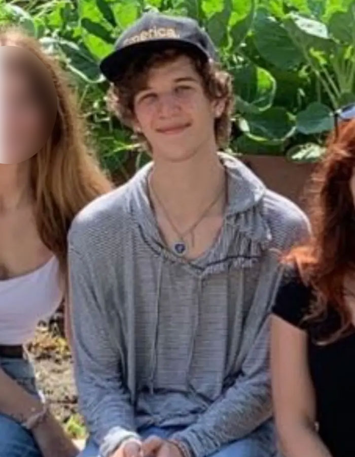 Teenage boy wearing a black cap and gray hoodie sitting outdoors with blurred person, related to Minneapolis Catholic School suspect. Teenage boy wearing a black cap and gray hoodie sitting outdoors with blurred person, related to Minneapolis Catholic School suspect.