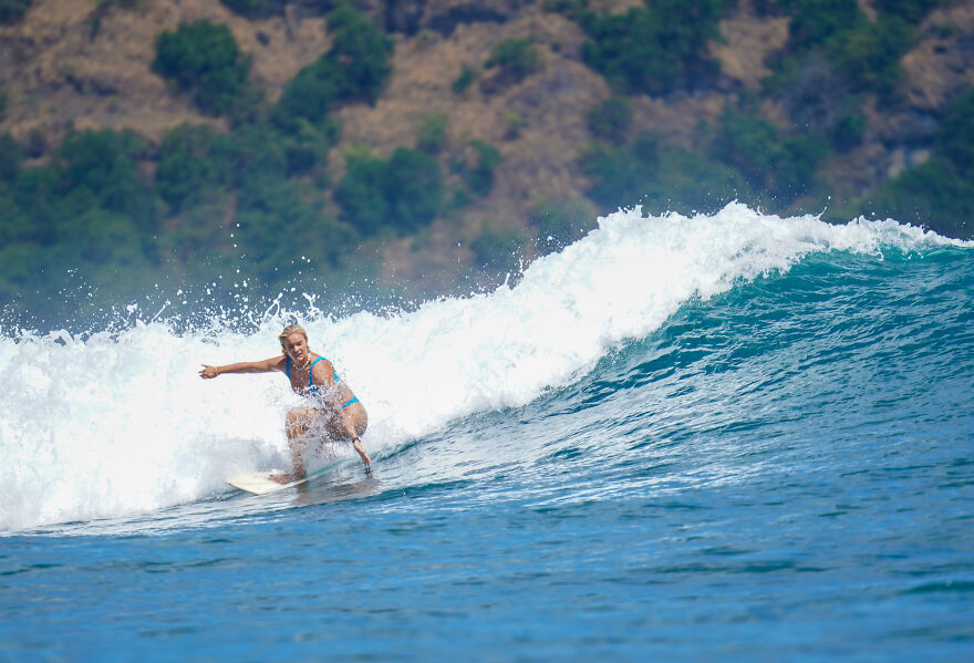 Woman surfing a large wave near a forested coastline, symbolizing a one-way flight to Australia life transformation.