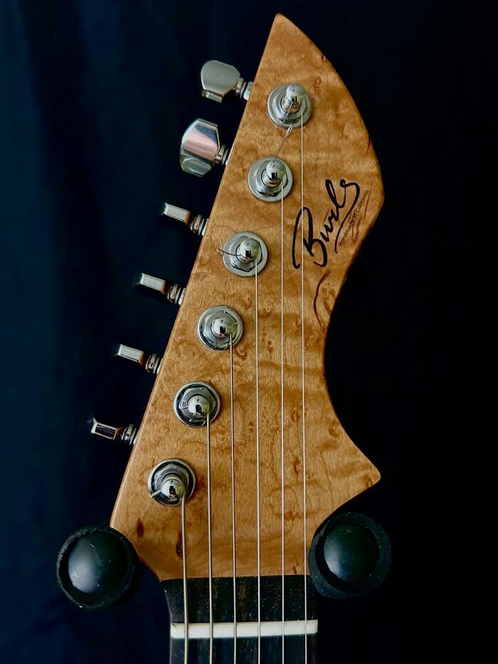 Close-up of a guitar headstock crafted using a 3D mold from stacks of newspapers, showcasing detailed wood grain.