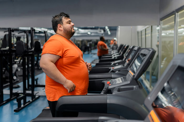 Overweight man wearing an orange shirt using treadmill in gym highlighting healthier rival to Ozempic with no side effects. Overweight man wearing an orange shirt using treadmill in gym highlighting healthier rival to Ozempic with no side effects.