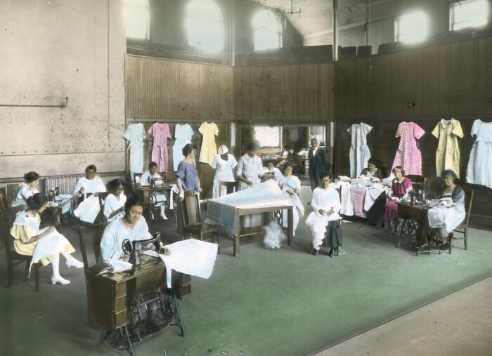African American women sewing and working with vintage sewing machines in a 1920s workshop, colorized photo.