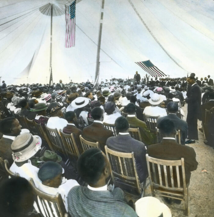 Large gathering of African American men and women under a tent, showcasing 1920s community life and culture.