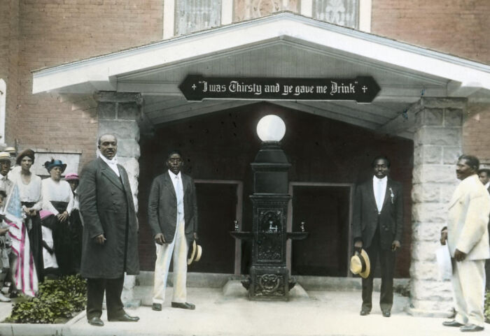 Group of African American men and women in 1920s attire standing outside a building, colorized photo showing African American reality.
