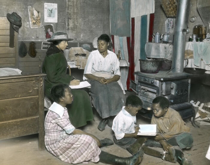 African American family in the 1920s sitting indoors by a stove, with children reading and adults engaged in conversation.