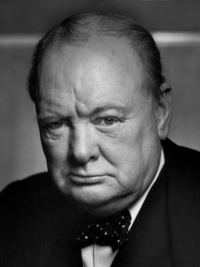 Black and white close-up portrait of a man in a suit illustrating savage roasts and comebacks with a serious expression.