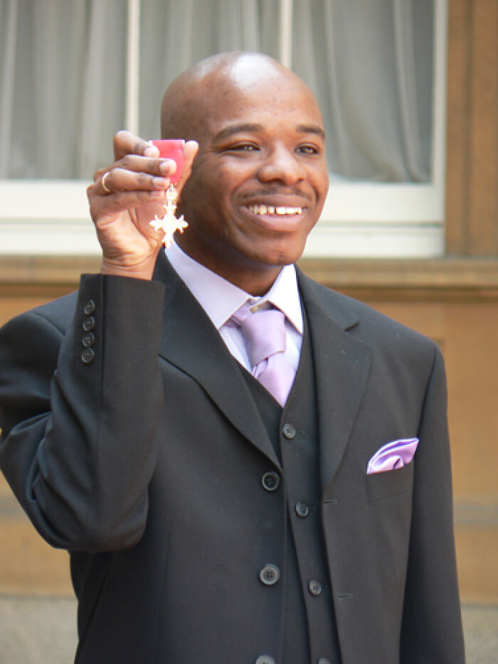 Smiling man in a suit holding a medal, representing proof that superhumans walk among us in an inspiring moment.