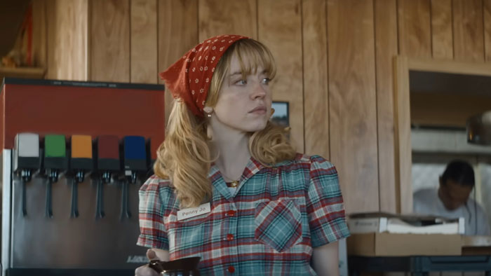 Woman in plaid shirt and red bandana looking aside in rustic diner scene for Sydney Sweeney new movie flop amid backlash. Woman in plaid shirt and red bandana looking aside in rustic diner scene for Sydney Sweeney new movie flop amid backlash.