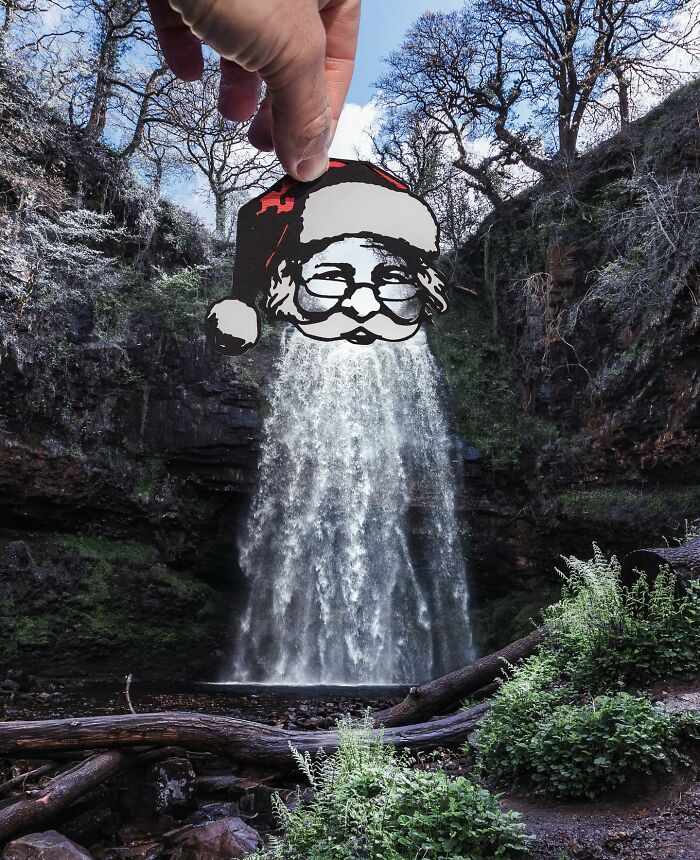 Hand holding paper cutout of Santa Claus over a waterfall, artist creates surprising scenes with paper cutouts worldwide.