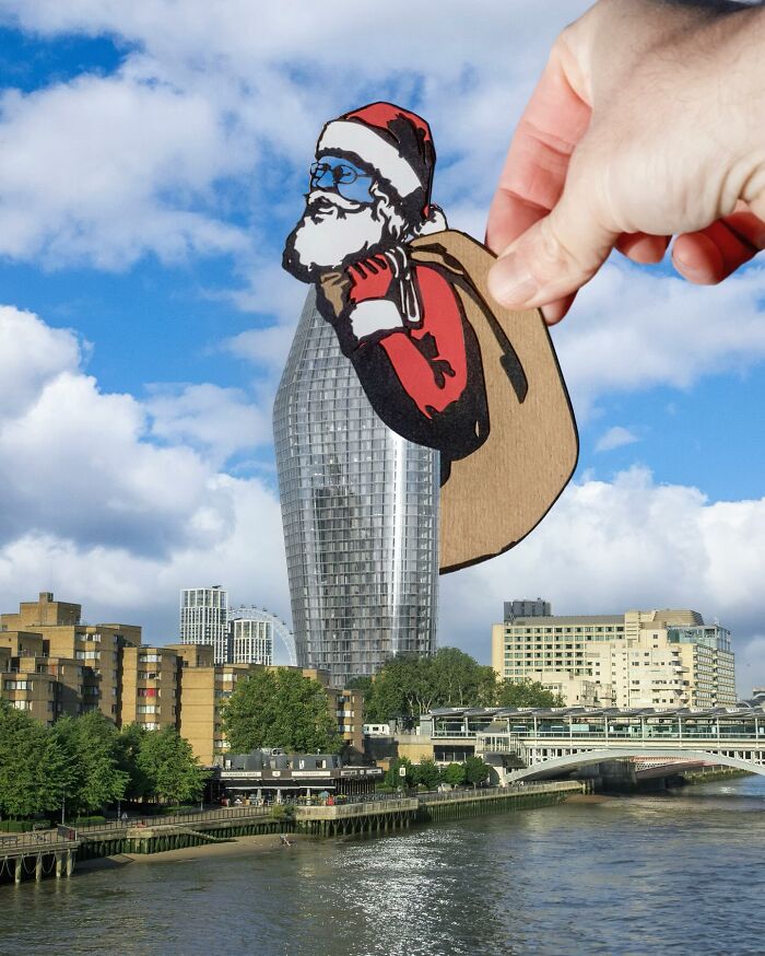 Hand holding a paper cutout of Santa Claus over a cityscape, showcasing artist travels and creative paper cutout scenes.