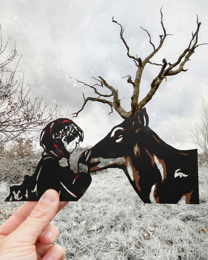 Hand holding paper cutout of a girl and a deer with tree branches as antlers, showcasing artist's creative travel scenes.