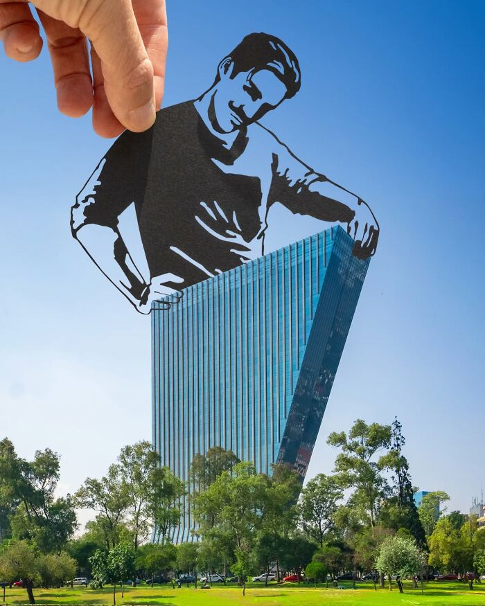 Hand holding a paper cutout of a man appearing to adjust a tilted modern building, showcasing artist travels the world with paper cutouts.