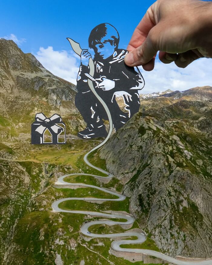Hand holding paper cutout of a boy with bow, combined with winding mountain road in a creative artist travel scene.