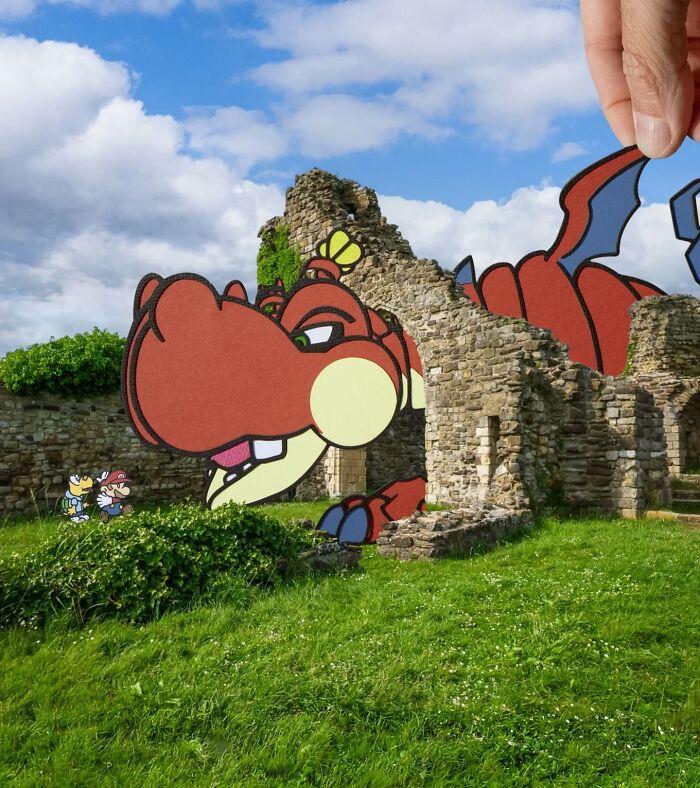 Hand holding paper cutout of a dragon and characters integrated into a real stone ruin scene by artist traveling the world.