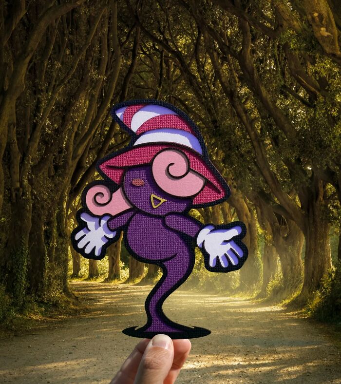 Hand holding a colorful paper cutout character in a sunlit forest path, showcasing artist's travels with paper cutouts.