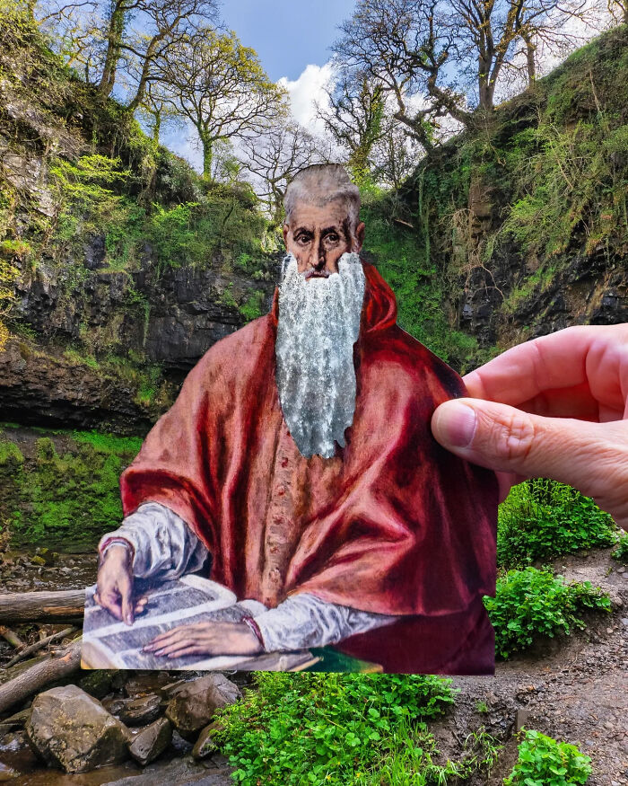 Hand holding paper cutout of an old man with a waterfall beard in a lush natural outdoor setting, artist travels the world.
