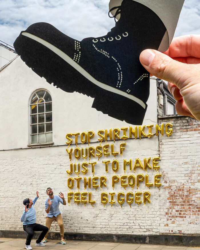 Hand holding paper cutout of a large boot over two men against a wall with balloon letters in a creative paper cutout art scene.