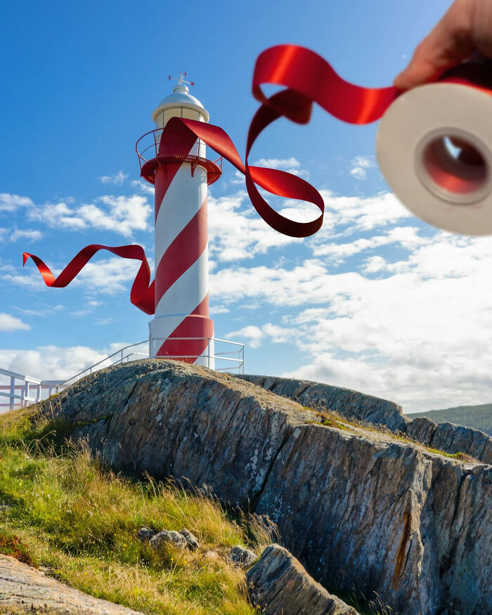 Lighthouse on rocky shore with red paper cutout ribbon artistically integrated into the scene during daytime.