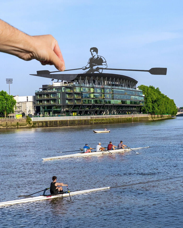 Hand holding paper cutout of a rower placed over a riverside scene with people rowing, showcasing artist paper cutouts creativity.