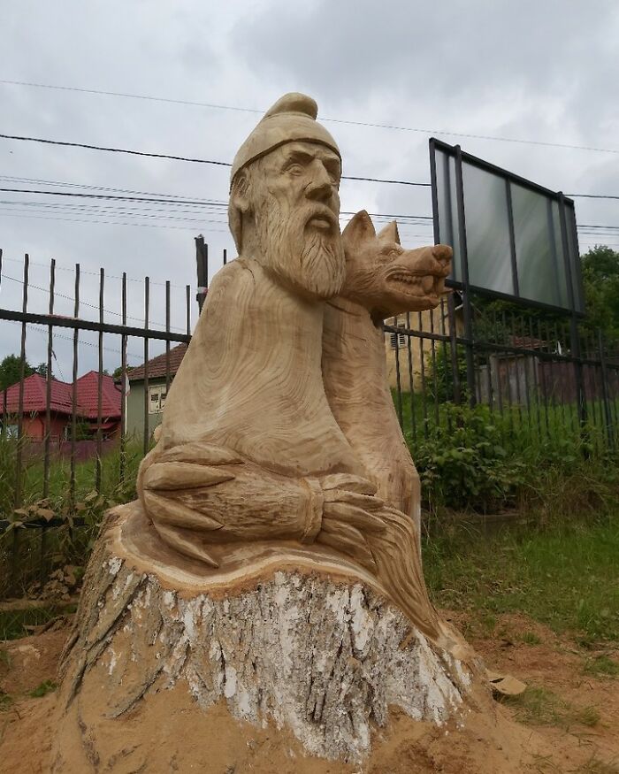 Wooden sculpture of a bearded man and a dog carved by a chainsaw artist transforming forgotten trees into art outdoors.