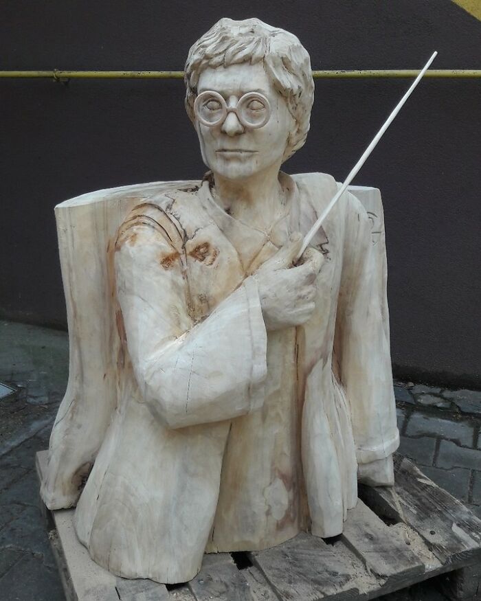 Wooden sculpture of a person with glasses holding a wand, showcasing chainsaw artist transforming forgotten trees into art.