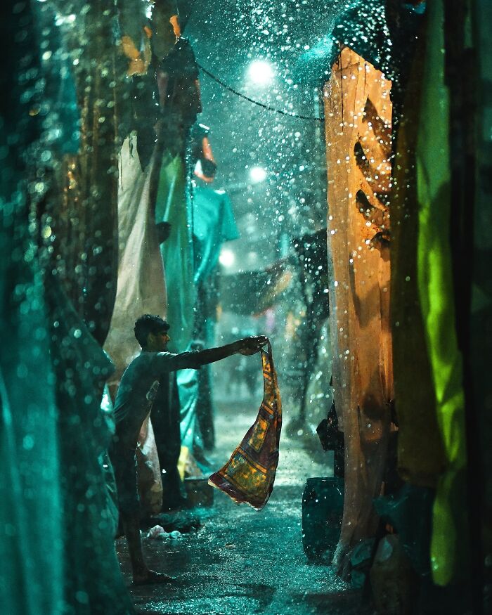 Man drying colorful fabric in rain-soaked vibrant street, showcasing vivid photos of India bursting with color and life.