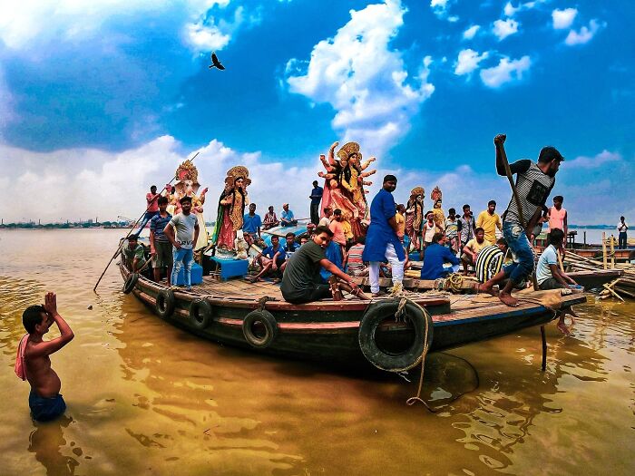 Boat carrying colorful religious statues on river with people, vibrant scene reflecting vivid photos of India bursting with color and life