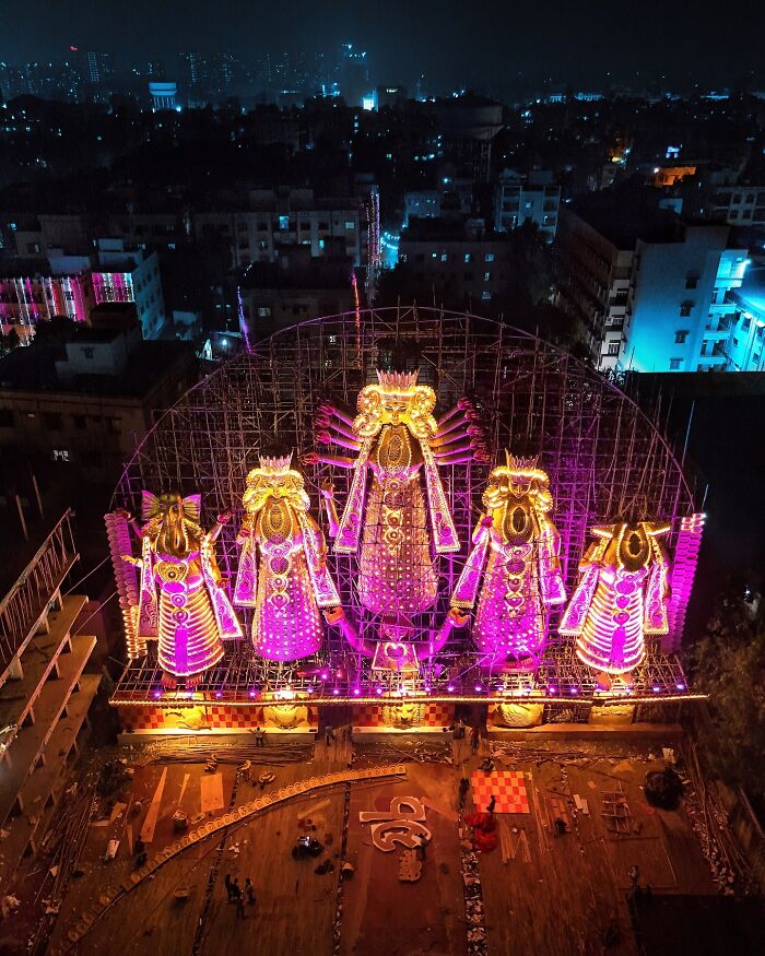 Vivid nighttime photo of illuminated Indian festival statues glowing in bright pink and yellow lights in a vibrant cityscape.