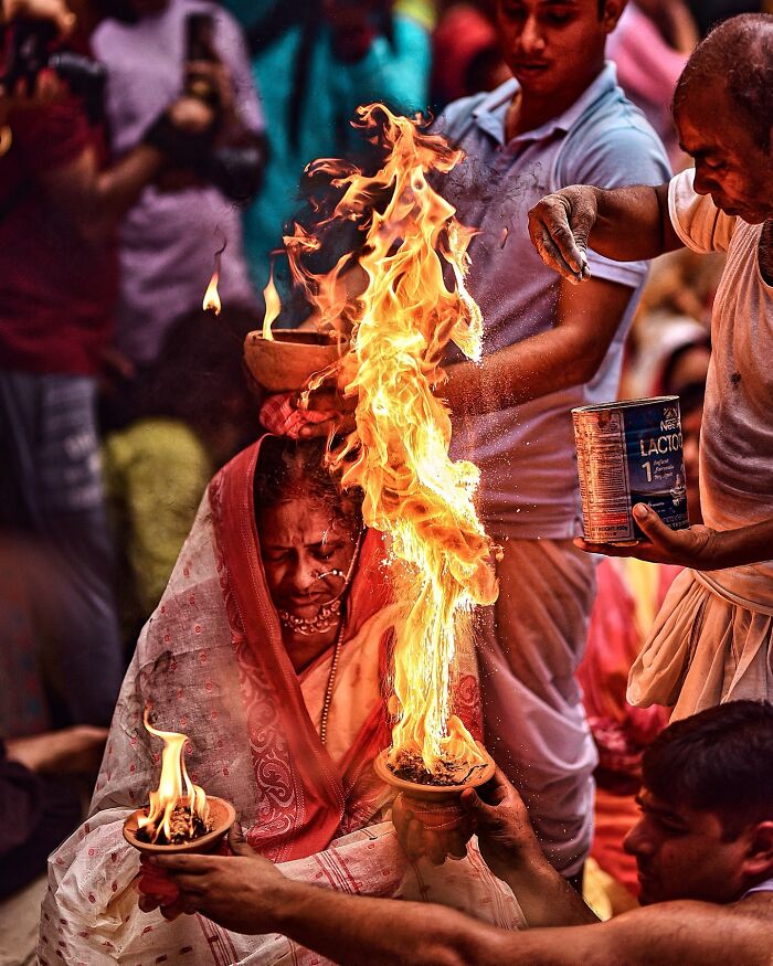 Woman in traditional attire participating in a vibrant Indian fire ritual, surrounded by people during a cultural ceremony.