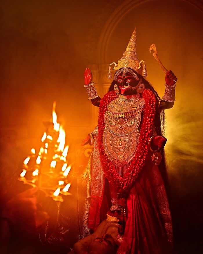 Vivid photo of a colorful Indian goddess statue adorned with intricate jewelry and surrounded by warm, glowing flames.