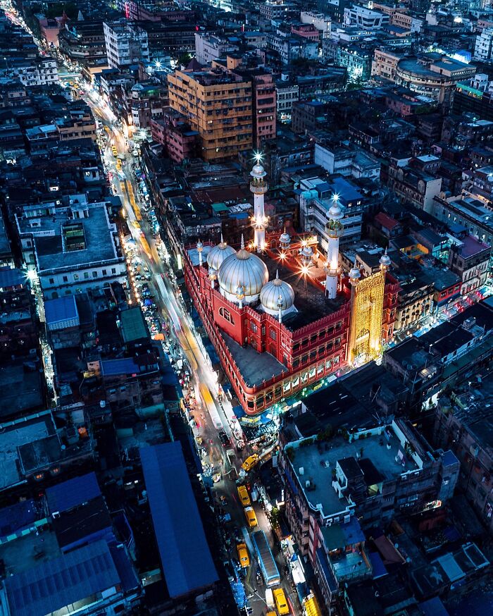 Aerial night view of a vibrant city in India with illuminated historic architecture and busy streets full of life.