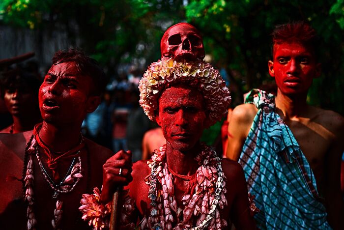 Men covered in red powder and adorned with floral garlands and a skull during a vivid cultural festival in India bursting with color and life.