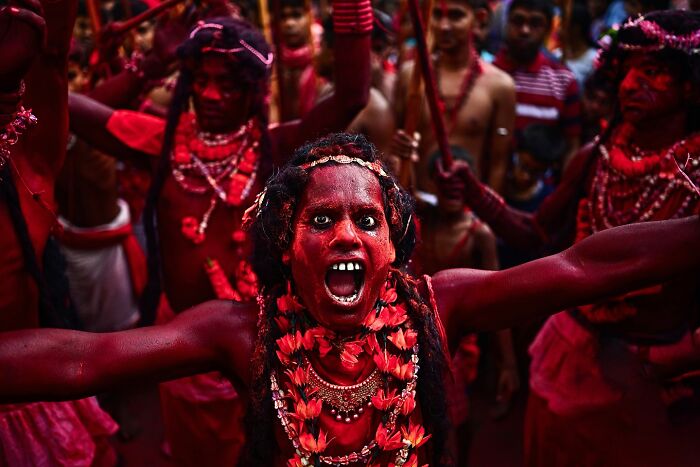 Man covered in red powder with floral garlands and traditional attire, captured in vivid India photo bursting with color and life.