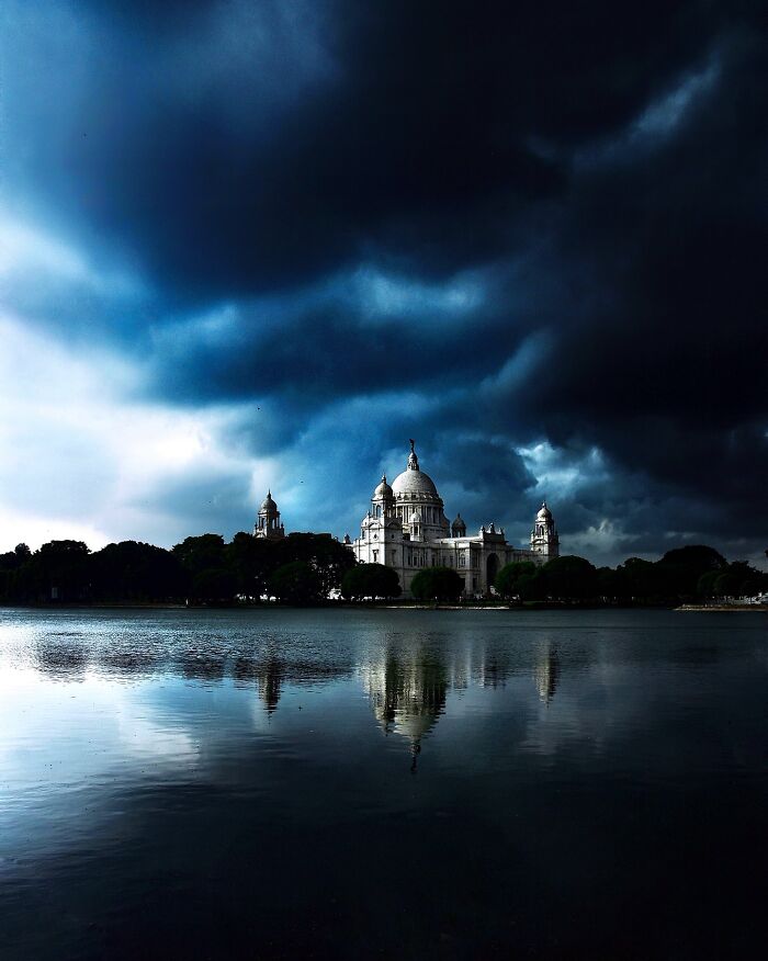 Victoria Memorial in India under dramatic stormy sky with vivid reflections on water showcasing color and life.