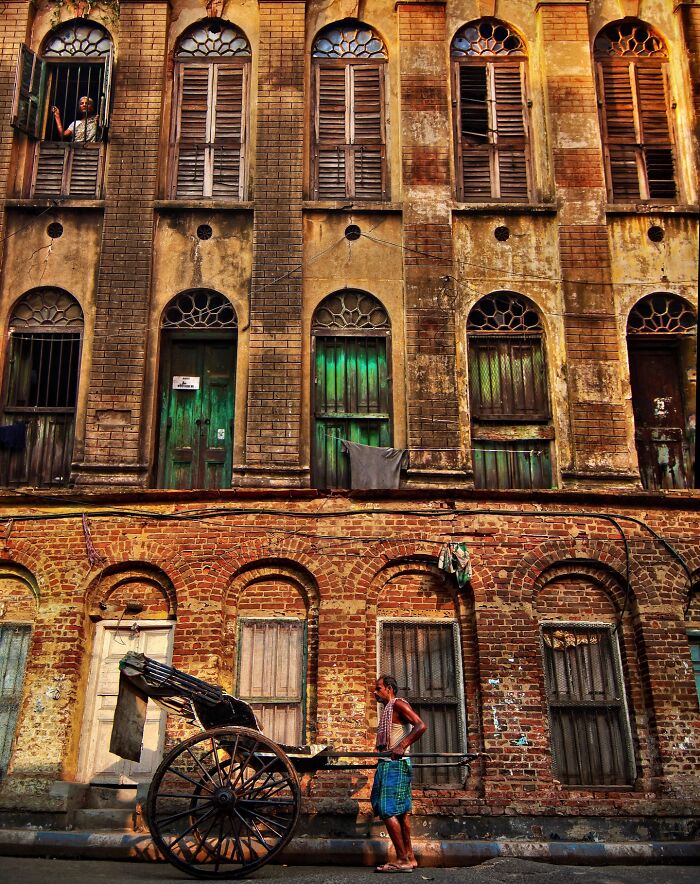 Rickshaw puller standing in front of an old weathered building, showcasing vivid colors and life in India street scenes.