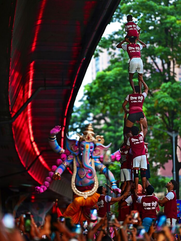 Human pyramid forming during a vibrant India festival with colorful Ganesh idol in the background, bursting with color and life.