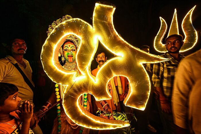 A vibrant Indian cultural celebration at night with illuminated symbols and people in traditional attire.