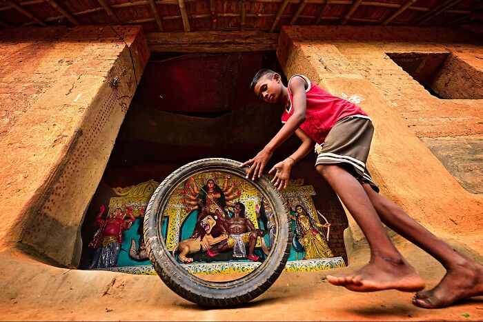 Young boy playing with a tire in front of colorful traditional Indian sculptures bursting with color and life.