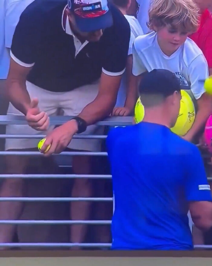 Polish CEO caught at US Open reaching for a fan's hat, surrounded by tennis balls and spectators. Polish CEO caught at US Open reaching for a fan's hat, surrounded by tennis balls and spectators.