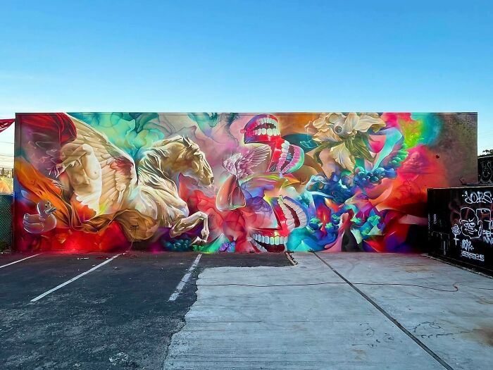 Colorful mural blending graffiti, realism, and abstraction with dynamic shapes, horses, flowers, and surreal elements in an outdoor parking lot.