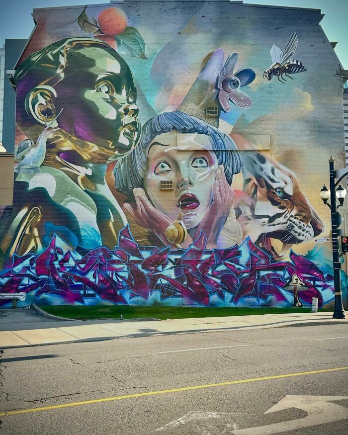 Colorful mural blending graffiti, realism, and abstraction featuring a baby, a surprised woman, and a tiger on an urban wall.