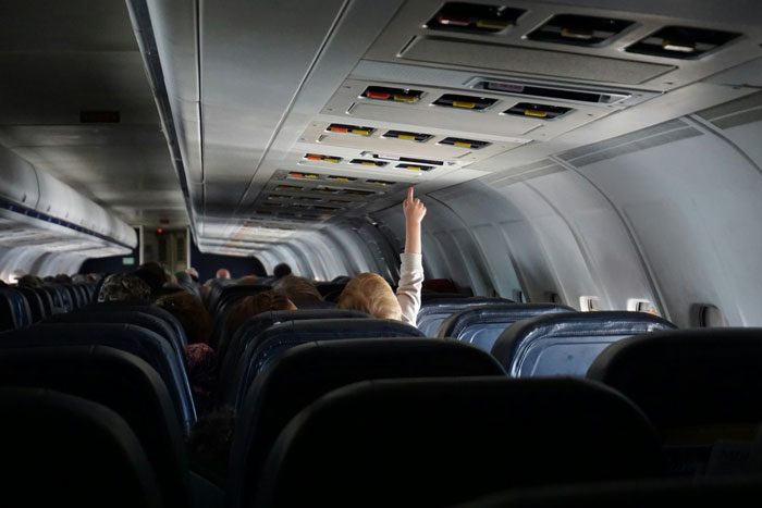 Passenger in airplane cabin raising hand during flight, illustrating extreme diarrhea leading to emergency landing and cancellation. Passenger in airplane cabin raising hand during flight, illustrating extreme diarrhea leading to emergency landing and cancellation.