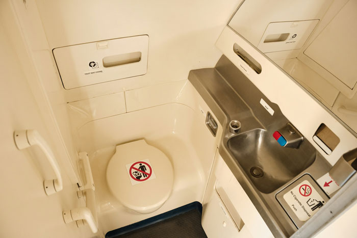 Airplane lavatory with closed toilet seat and stainless steel sink, highlighting extreme diarrhea emergency landing scenario. Airplane lavatory with closed toilet seat and stainless steel sink, highlighting extreme diarrhea emergency landing scenario.