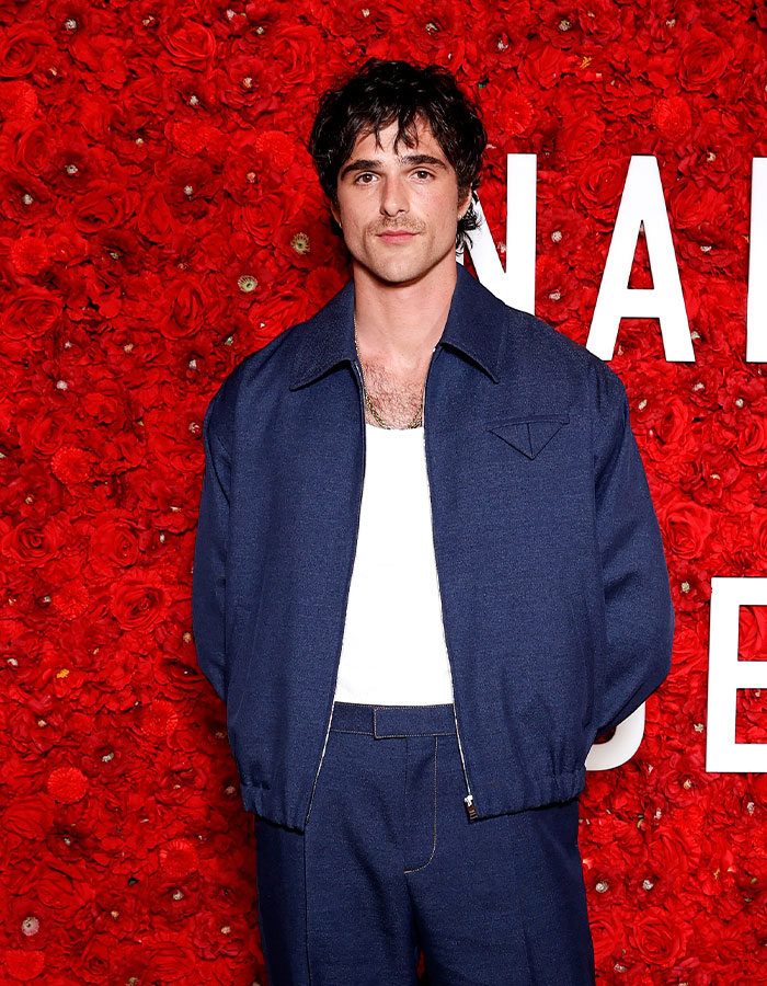 Actor posing in navy outfit against a red rose wall backdrop at event for controversial Wuthering Heights adaptation. Actor posing in navy outfit against a red rose wall backdrop at event for controversial Wuthering Heights adaptation.