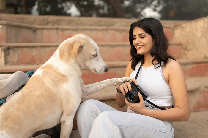 Woman holding a camera smiling at her light brown dog who is touching her hand outdoors on stone steps. Woman holding a camera smiling at her light brown dog who is touching her hand outdoors on stone steps.