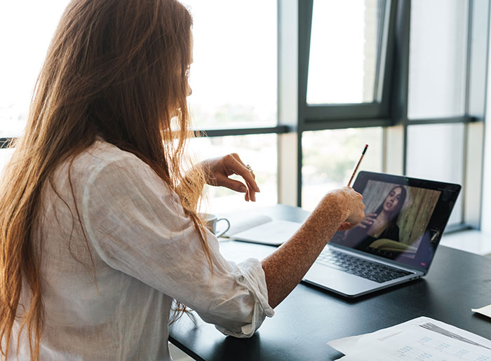Woman receiving an email about a second interview while watching a video file on her laptop at a desk near a window. Woman receiving an email about a second interview while watching a video file on her laptop at a desk near a window.