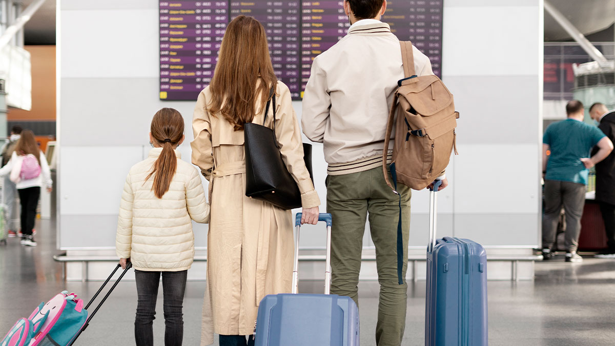 Family with luggage at airport looking at flight schedule, representing six-leg flight with a kid that traumatized a mom online vent.